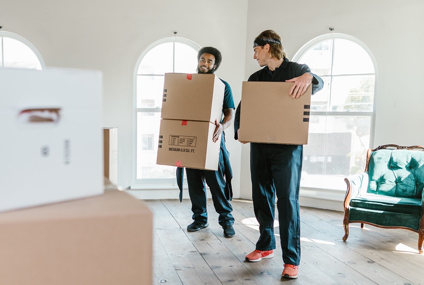 Movers carrying boxes in front of stacked boxes.