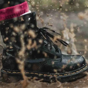 Black boot stepping in muddy puddle and splashing