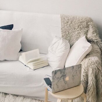 Laptop resting on stool facing an empty sofa with a blanket