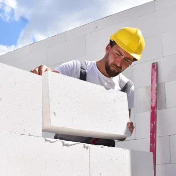 bricklayer with yellow hard hat laying white brick