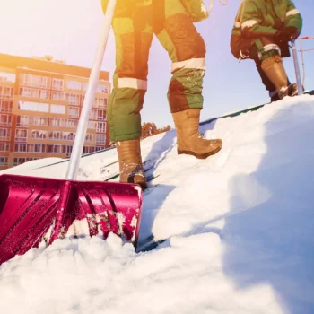 snow removal workers on roof clearing snow with shovel