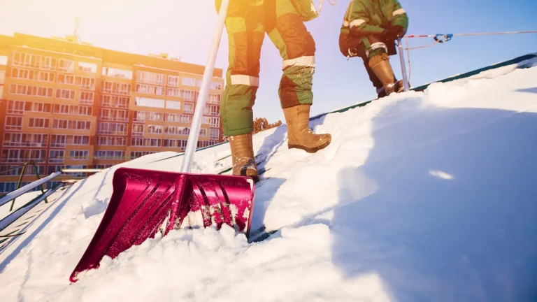 snow removal workers on roof clearing snow with shovel