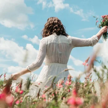 woman in white dress walking through field of wildflowers