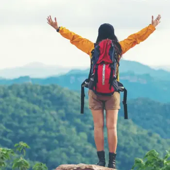 Woman standing on trail wearing backpack.