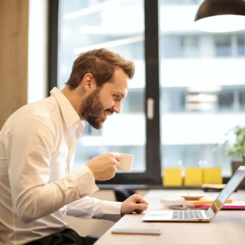 professional male working on desk on laptop drinking espresso