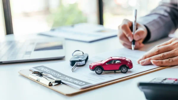 person signing lease contract with car key on paper