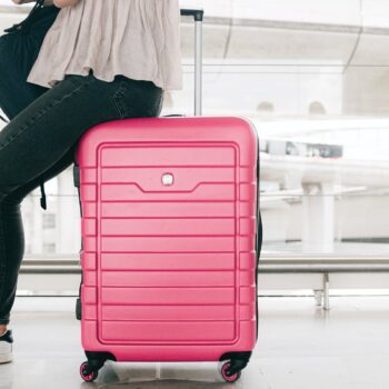 woman sitting on red suitcase in airport