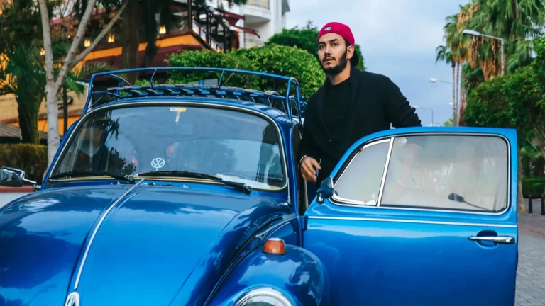 young man standing next to volkswagon beetle with door open