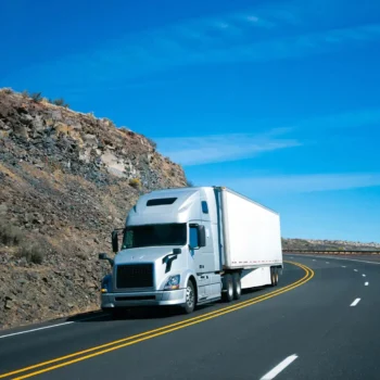 commercial transport truck driving on road next to rock face