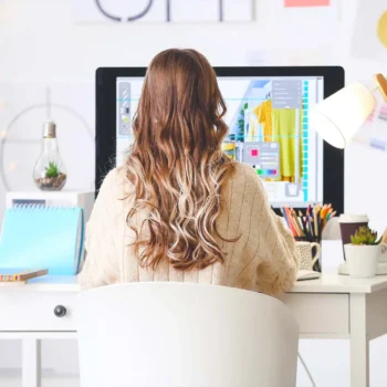 female with long blonde hair sitting at a computer desk working as a freelancer