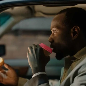 driver drinking coffee with pink lid while eating donut