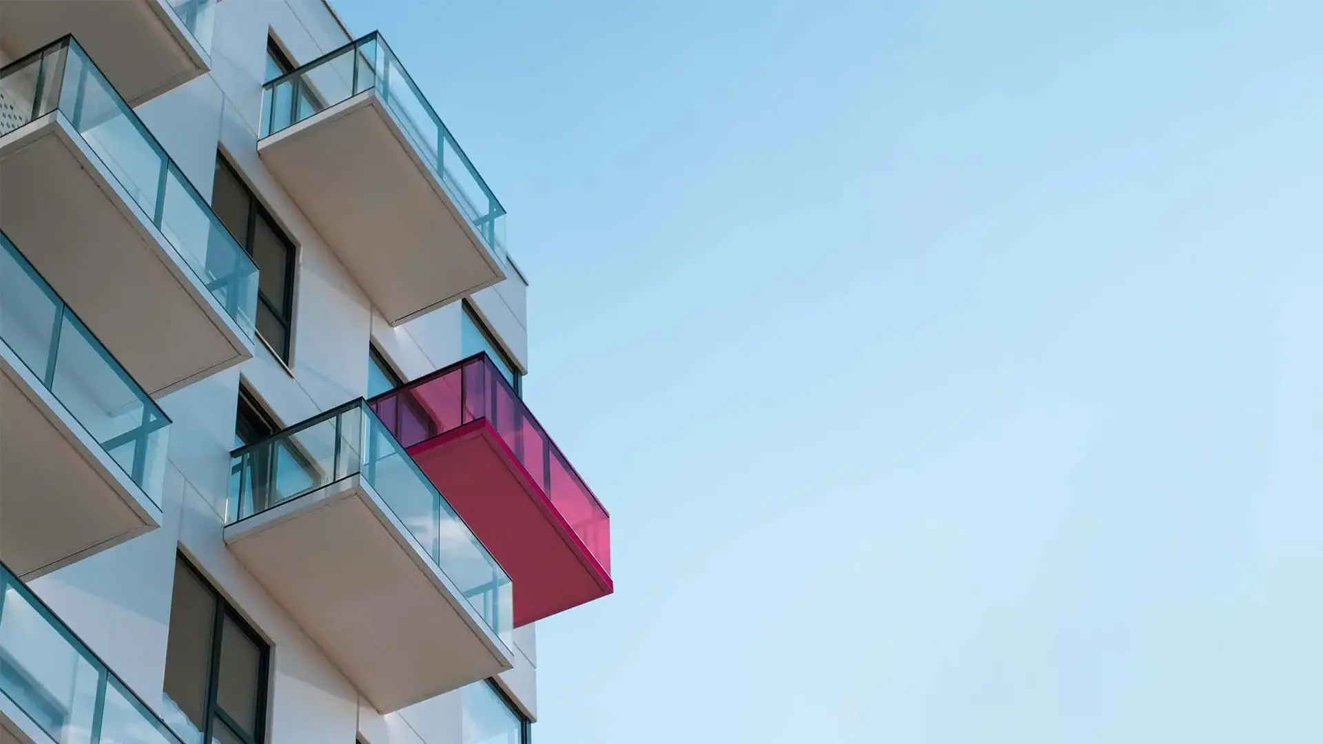 High-rise apartment building with glass balconies against a clear blue sky.