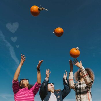 Three people throwing pumpkins in the air.