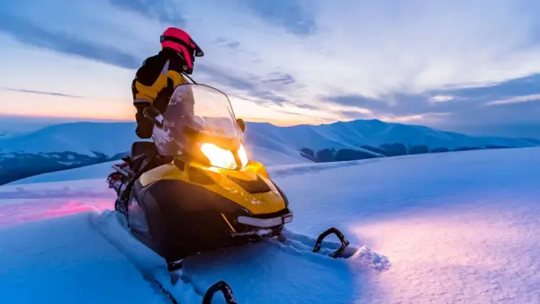 Snowmobile rider looking back at a snowy mountainous landscape.