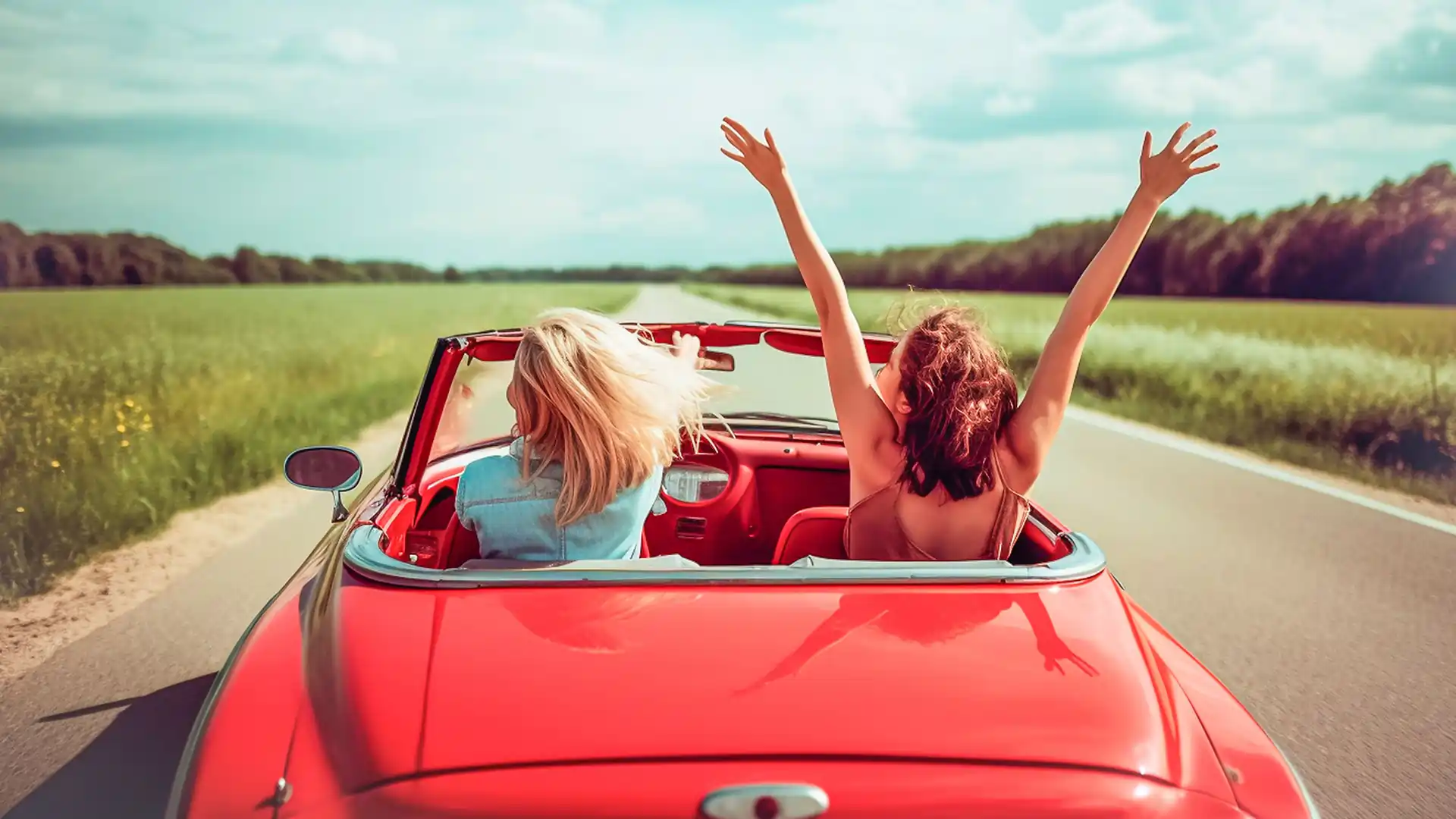 Two females driving in a convertible car through the country.